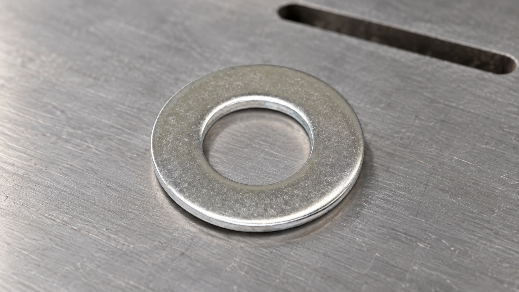 Close bearing-face view of a stainless steel flat washer on a supporting metal surface.